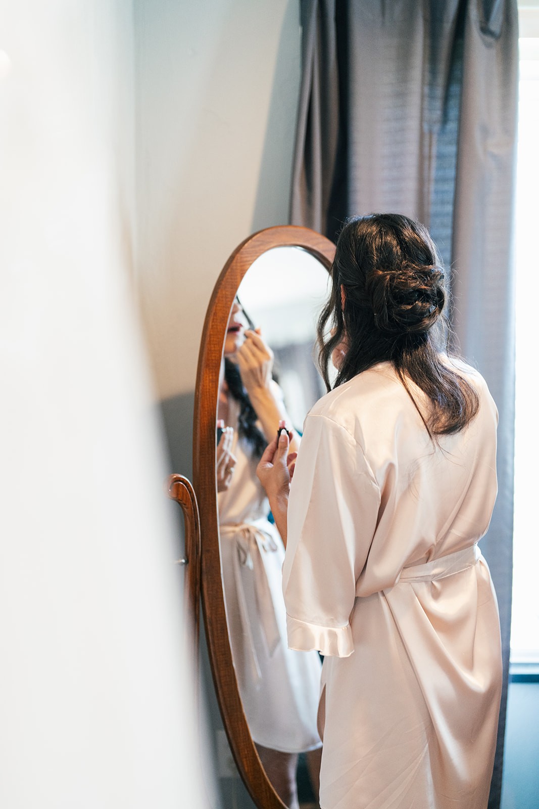 Danielle in a satin robe getting her makeup done before an oval mirror