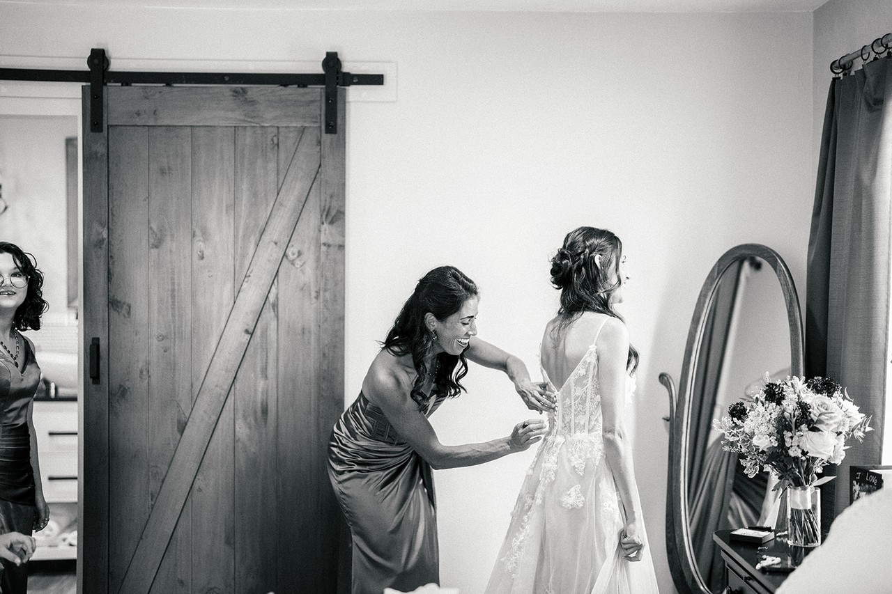 A helper fastens the back of Danielle's lace gown in the bedroom, black and white