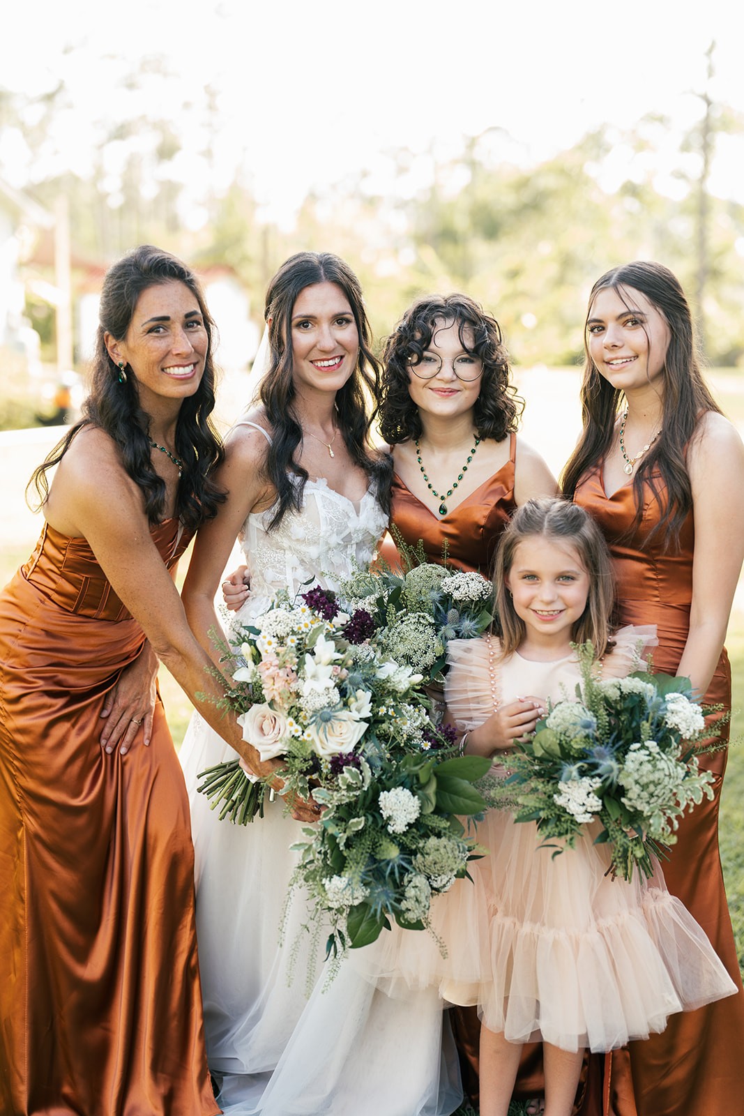 Danielle laughs with her bridesmaids in rust gowns and a young flower girl outdoors