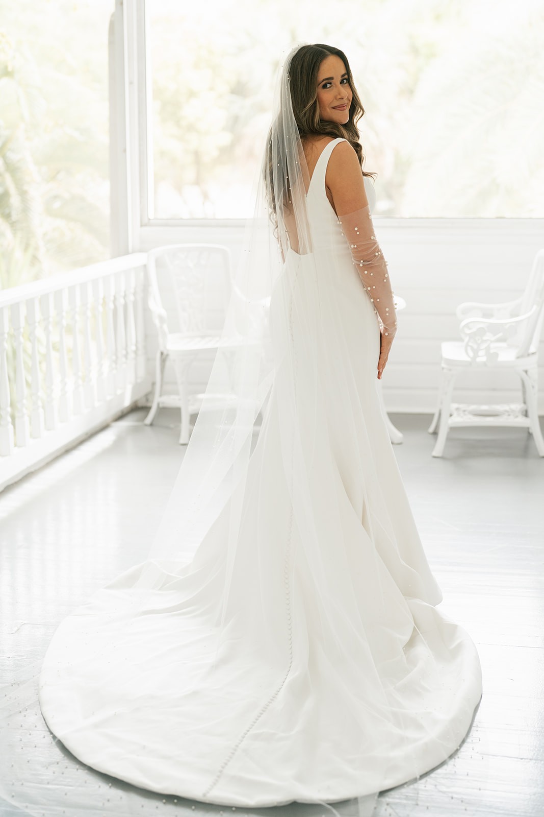 Chellsea glancing back over her shoulder, full gown and pearl veil flowing on a sunlit porch