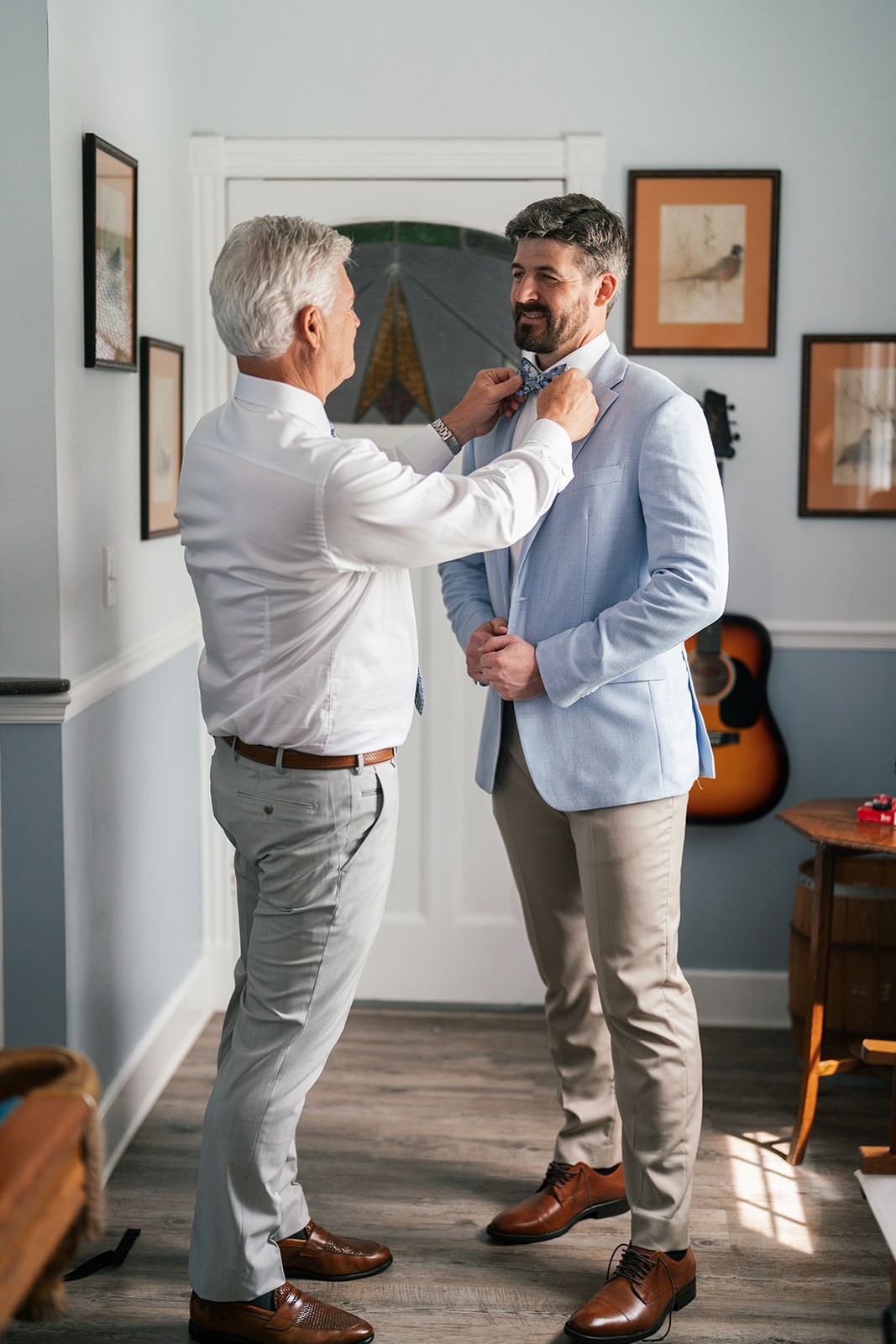 An older man helps Jacob with his bow tie as he buttons his blue jacket