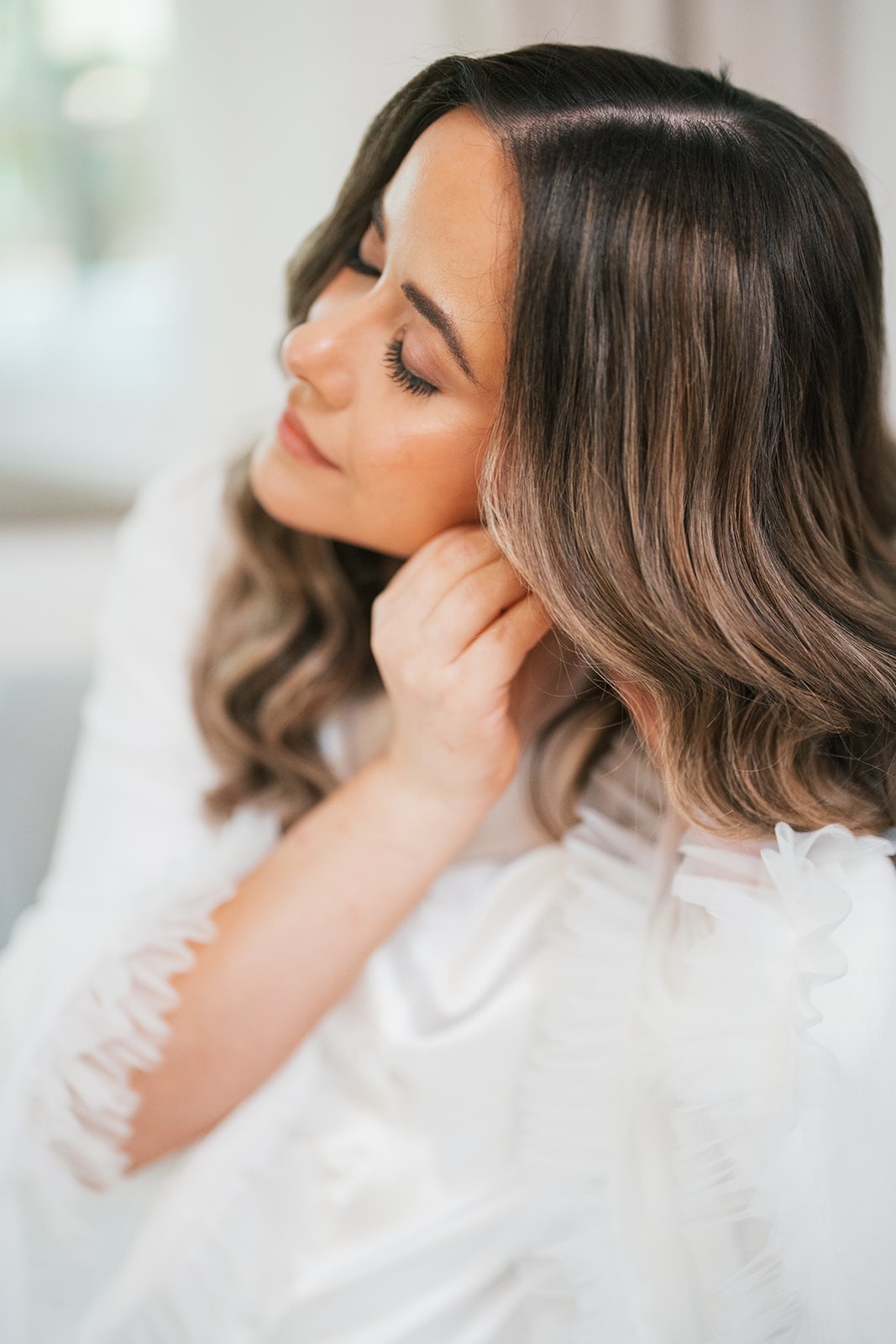 Chellsea in a white robe tucking her hair back during getting-ready in soft window light