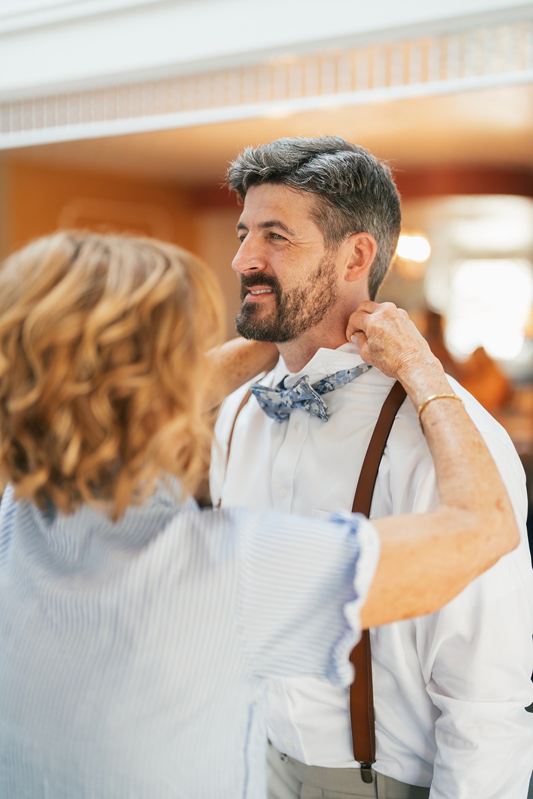 Jacob smiling as a woman helps tie his bow tie and suspenders