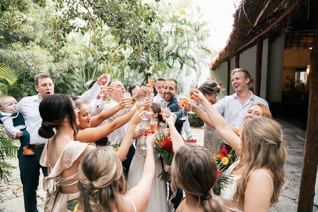 Wedding party raising glasses in a celebratory toast under tropical palms outdoors