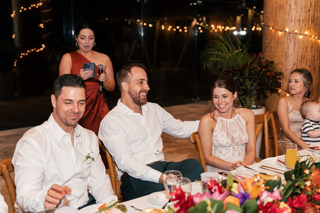 Brian laughing with guests around a flower-topped table at the evening reception