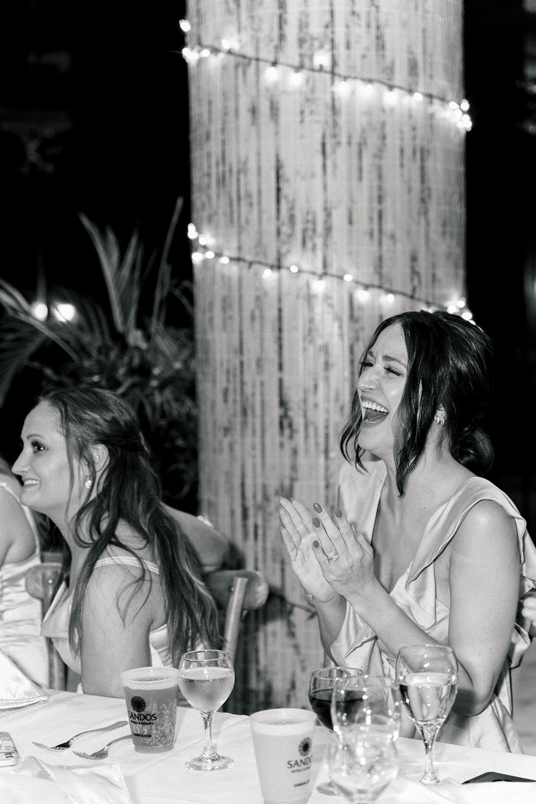 Black and white of a woman laughing and clapping at a candlelit reception table