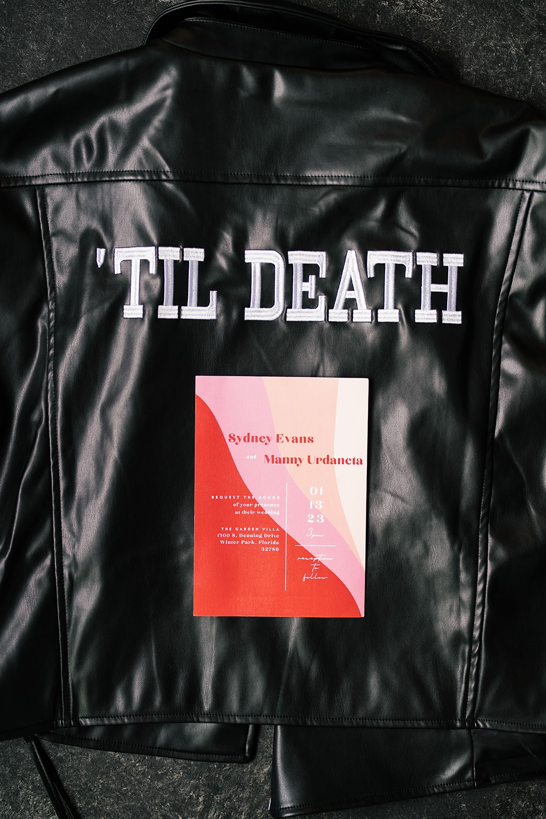 Sydney and Manny's wedding invitation resting on a black leather jacket embroidered with 'Til Death