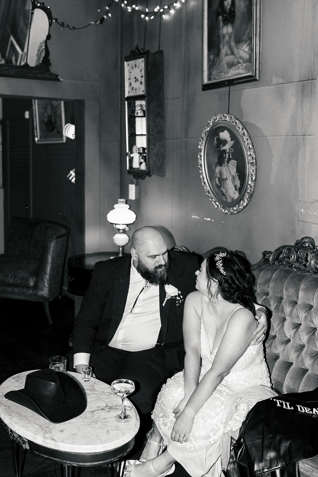 Black and white portrait of Sydney and Manny seated close together in a vintage lounge with framed art