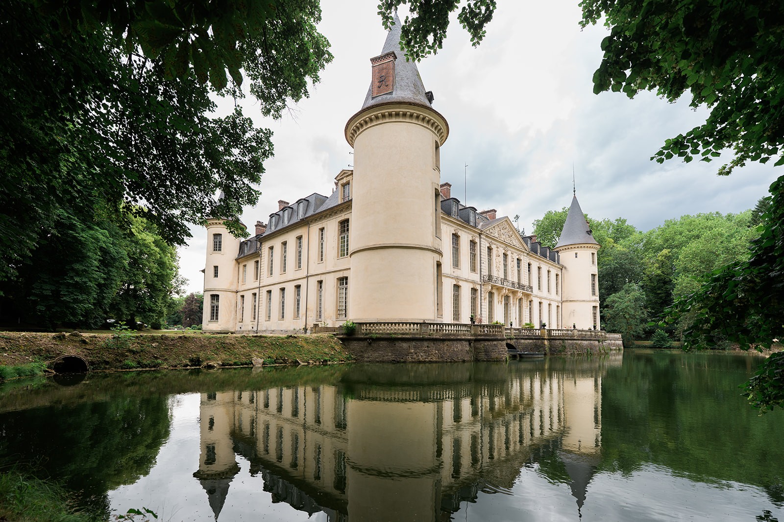 Domaine du Chateau d'Ermenonville and its turrets mirrored perfectly in the glassy moat, framed by green summer leaves