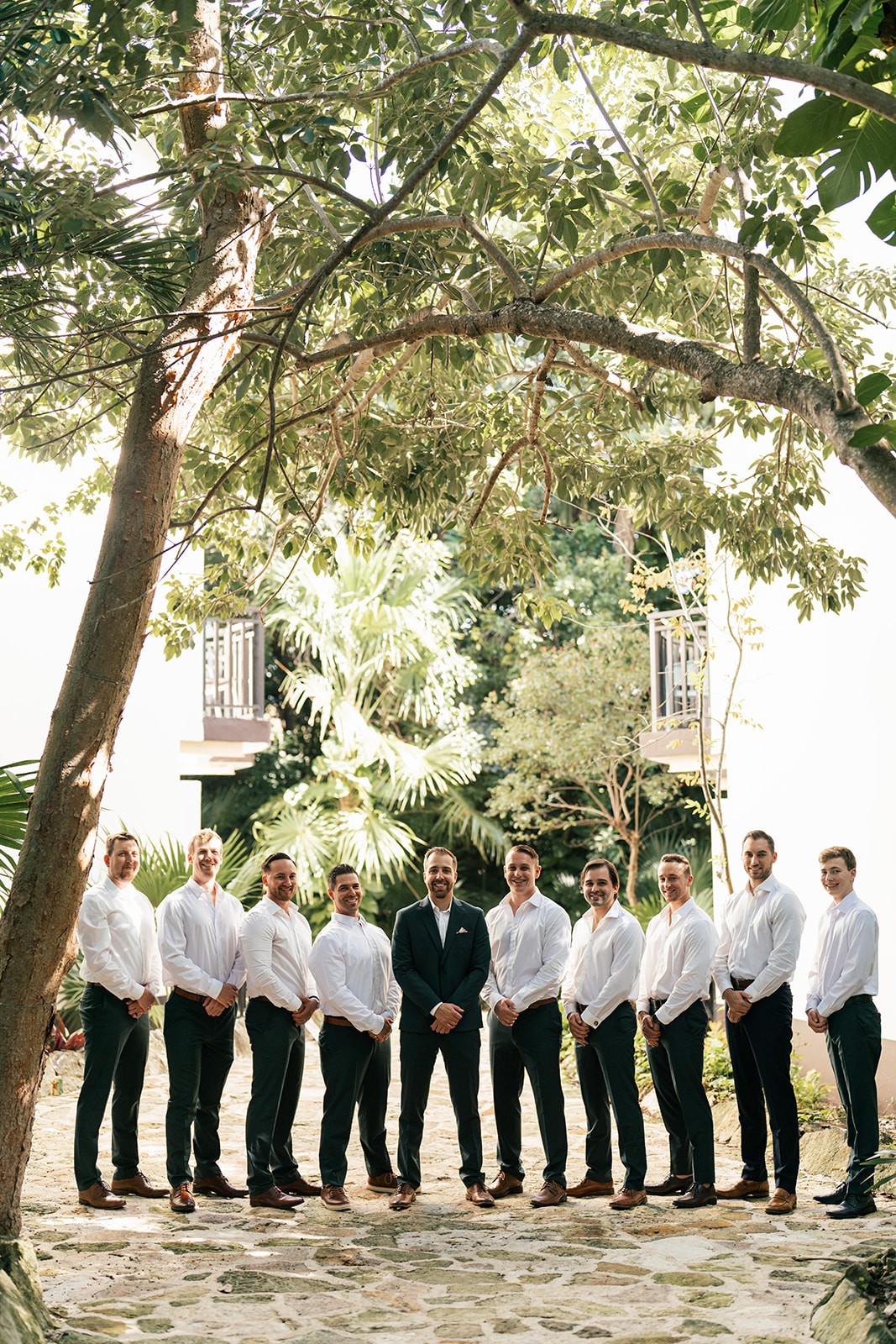 Brian and his groomsmen posing together beneath a sprawling tree in a courtyard
