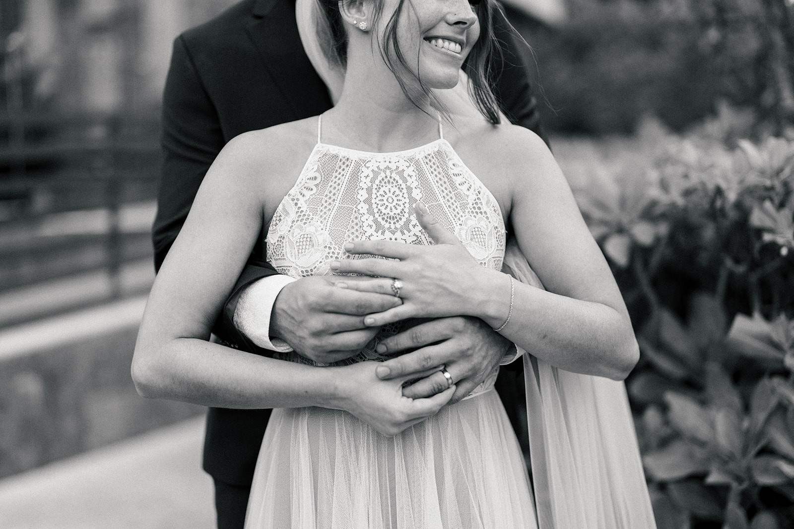 Black and white portrait of the bride smiling radiantly while the groom embraces her from behind in a tender moment.
