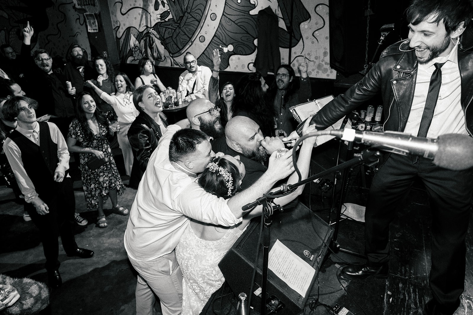 Black and white shot of the couple onstage with a band as guests cheer at the reception