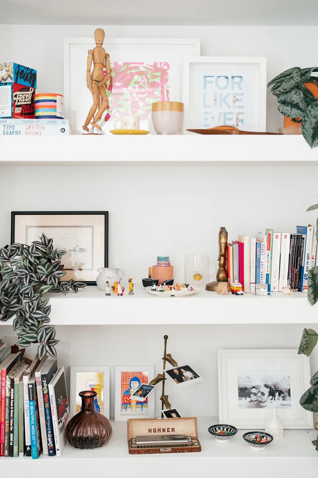 Three white shelves filled with books, framed art, and curated objects