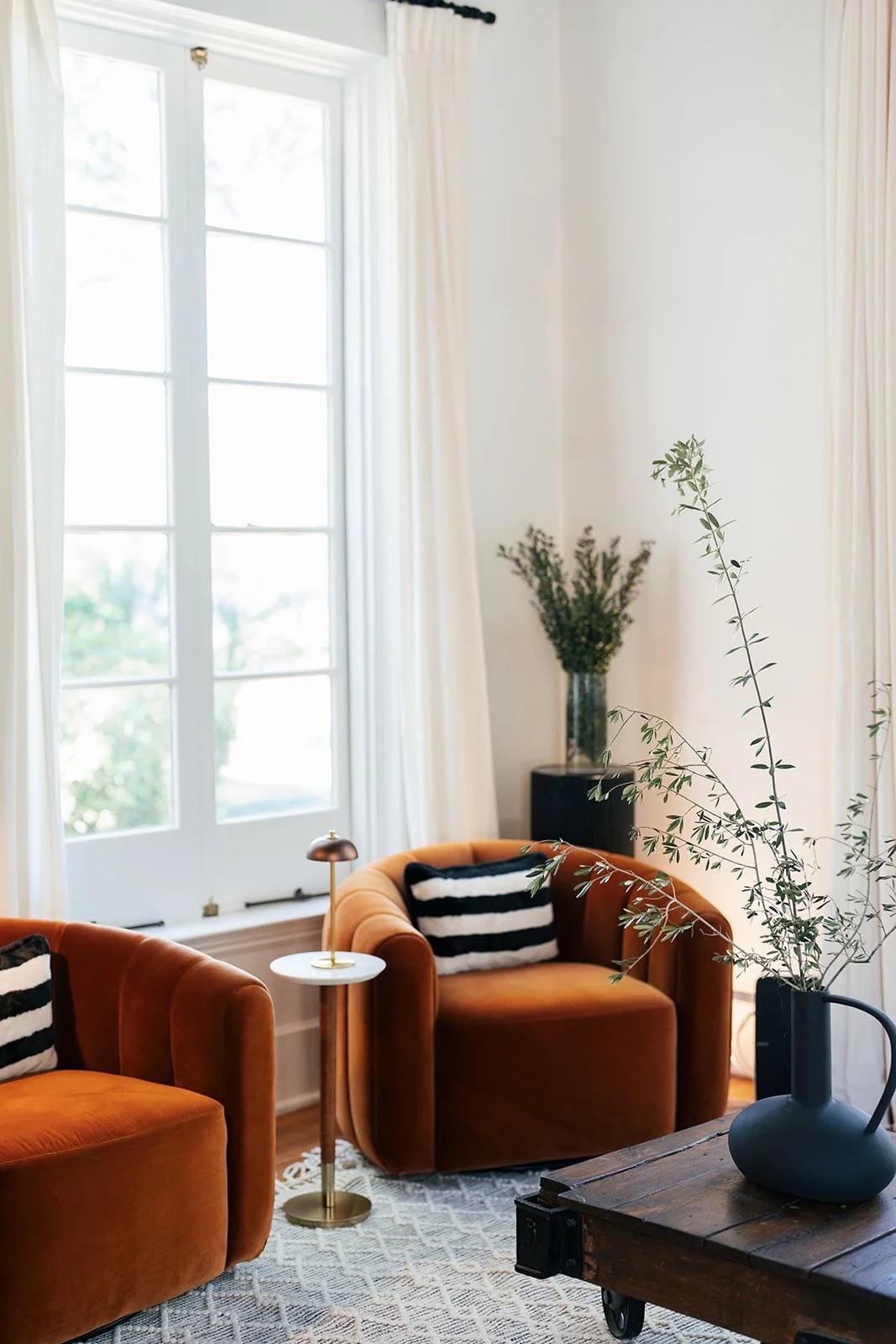 Living room with large window, white curtains, and orange velvet chairs