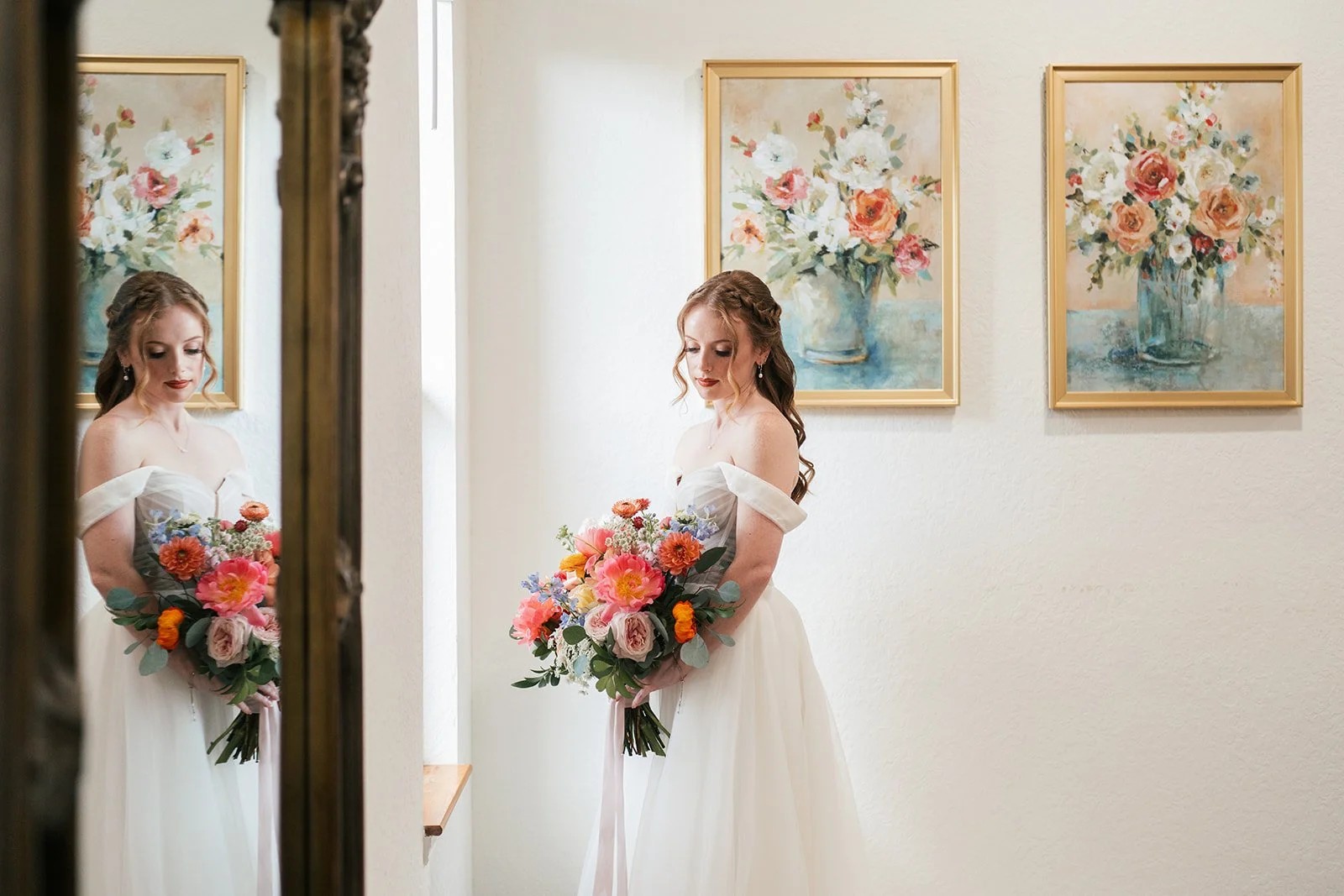 Bride holds a bright bouquet beside a mirror while getting ready