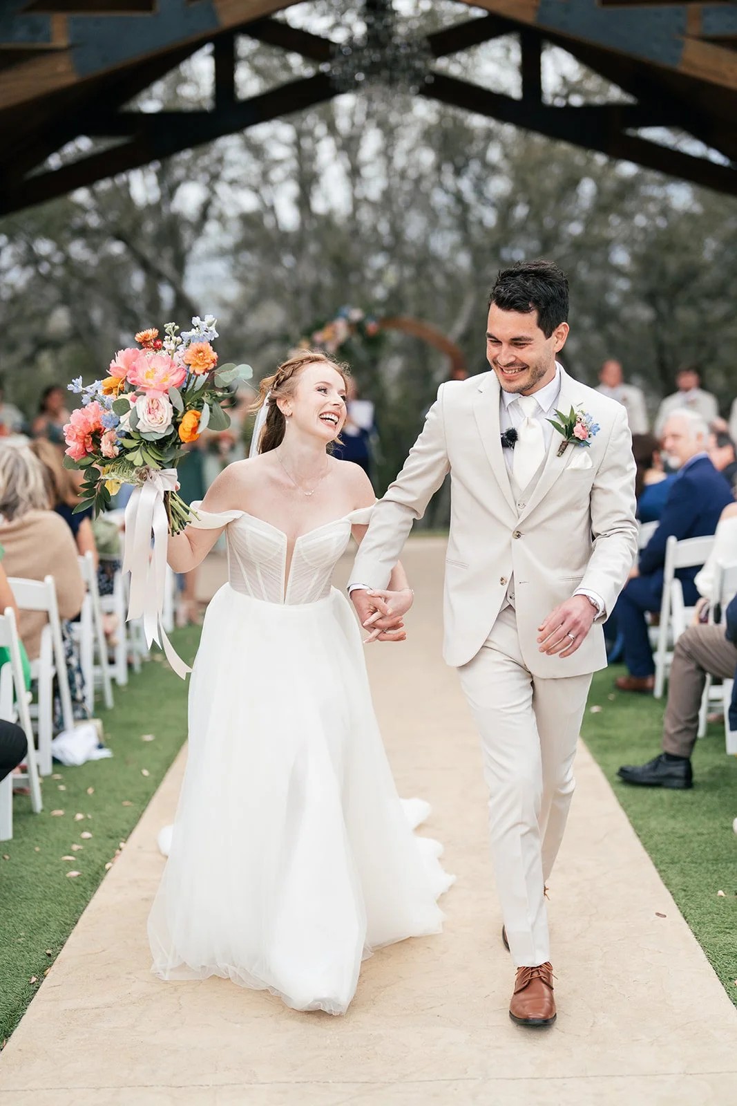 Bride and groom laugh while walking down the ceremony aisle hand in hand