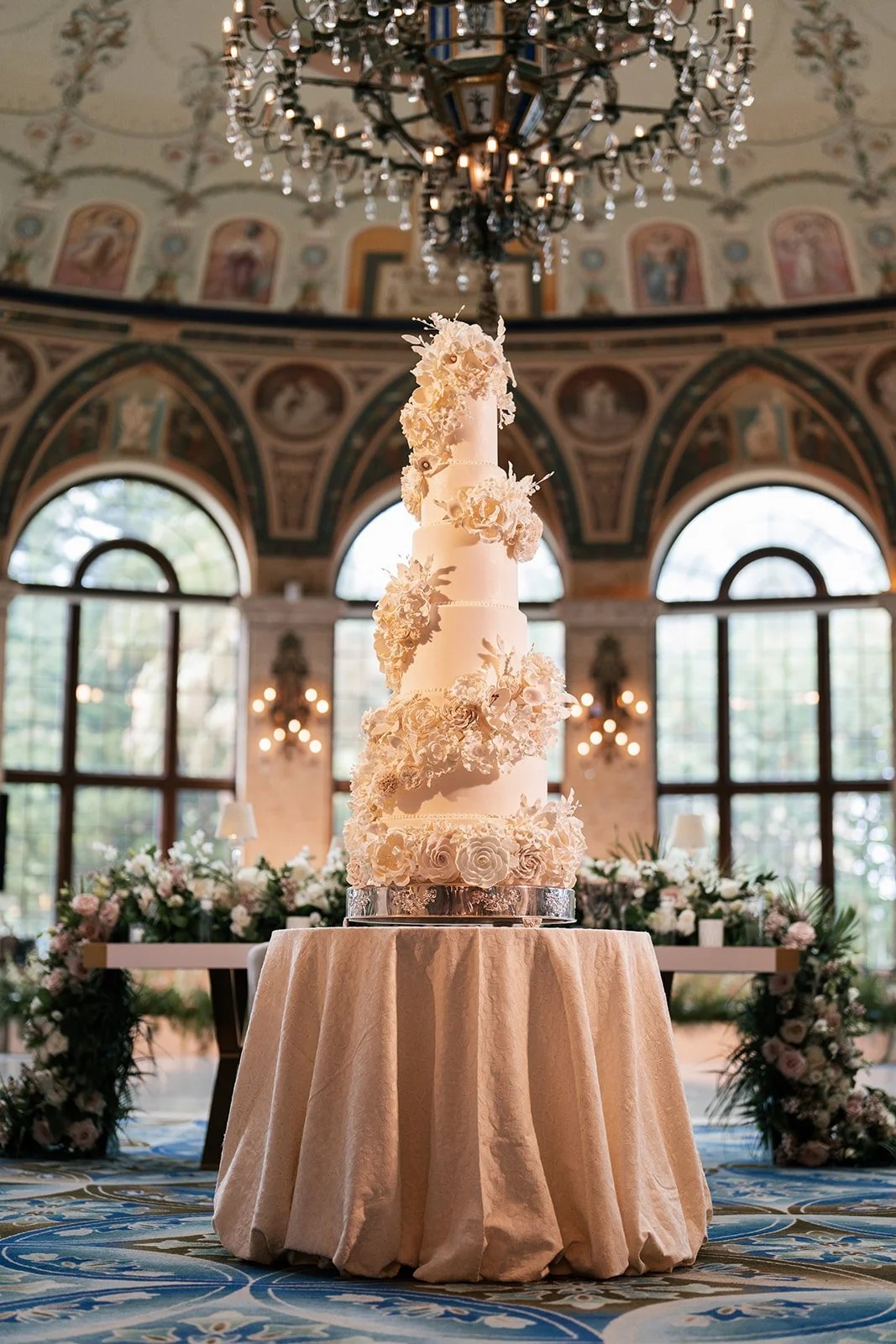 Towering ivory wedding cake with dried florals beneath a frescoed ballroom dome