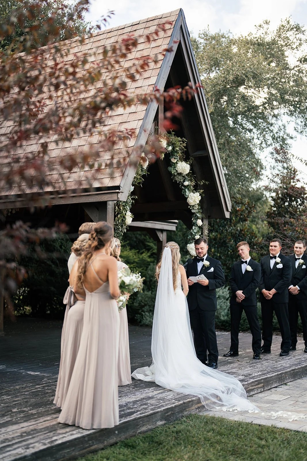 Couple reads vows beneath a wooden chapel with groomsmen looking on