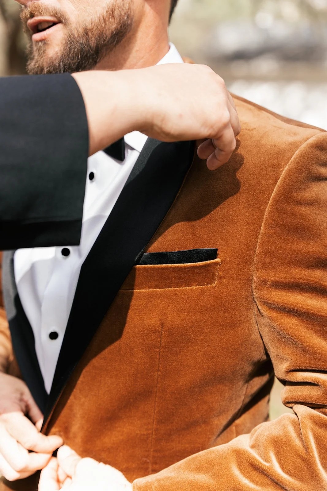 Close detail of groom buttoning rust-colored velvet tuxedo jacket
