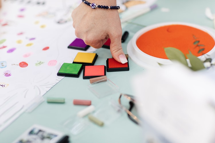 Close-up of a guest choosing colorful ink pads for a fingerprint guest book at the reception, a completed thumbprint tree visible to the left.
