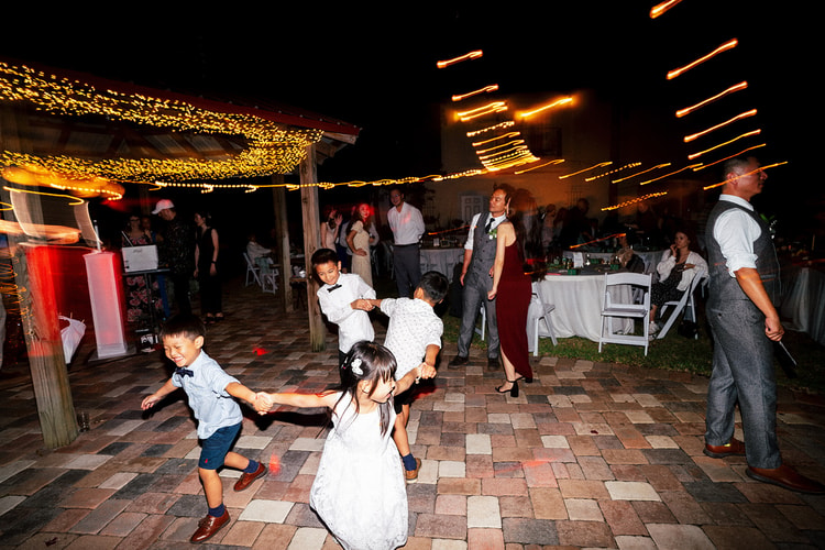Children running and spinning on the outdoor dance floor at night, string lights and fairy lights streaking overhead in a long-exposure blur.
