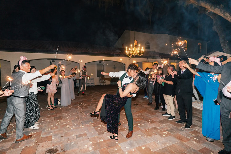 Sparkler send-off: groom dips the bride dramatically in the center of a circle of guests holding sparklers aloft against the night sky.