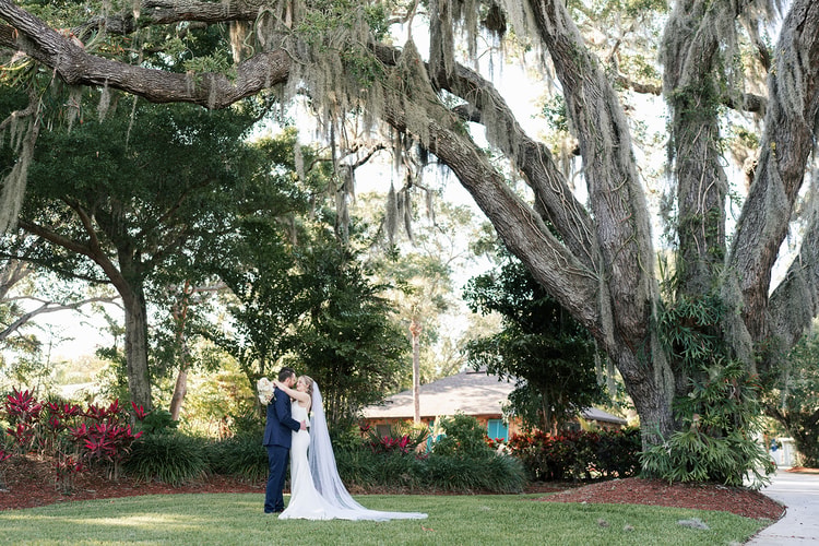 Couple embracing under a sweeping live oak draped with Spanish moss in the venue garden.