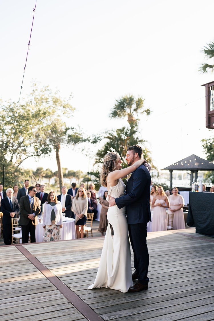 Bride and groom seated at the sweetheart table during dinner, the bride laughing while listening to a toast.