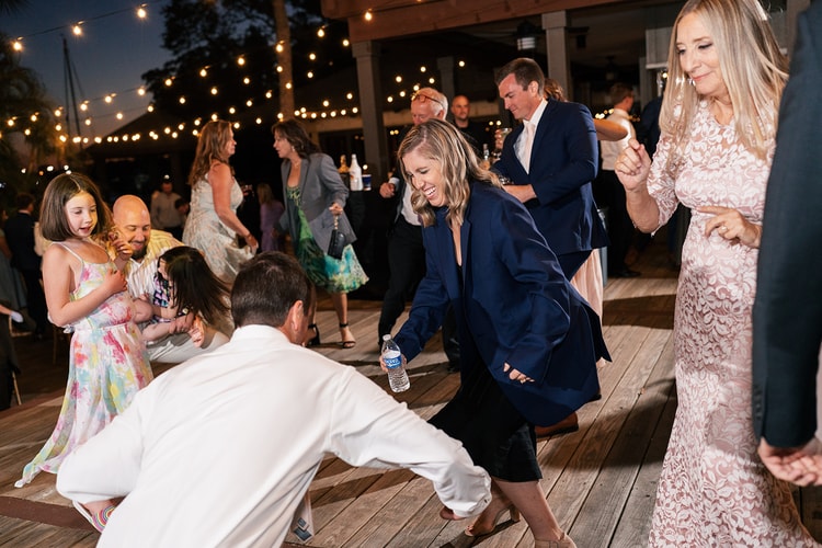 Guests of all ages dancing energetically on the outdoor deck reception floor under string lights.