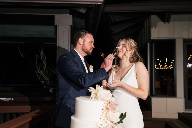 Groom feeds the bride a bite of wedding cake with a gold fork; she closes her eyes in delight as he smiles.