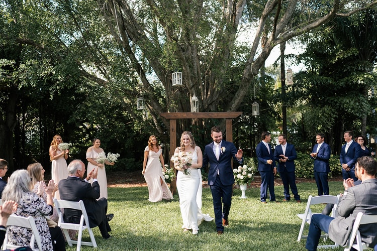 Newlyweds walk back up the aisle hand in hand after the ceremony, guests applauding on either side.