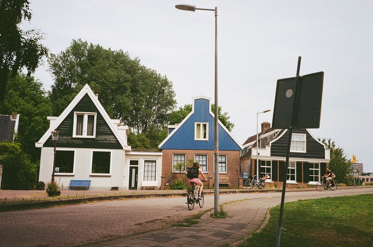 Cyclist riding past a row of colorful Dutch houses with white and blue architecture lining the residential street.