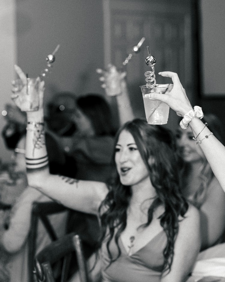 Black-and-white close-up of a guest raising a cocktail with a disco-ball straw while celebrating at the reception, wedding photography