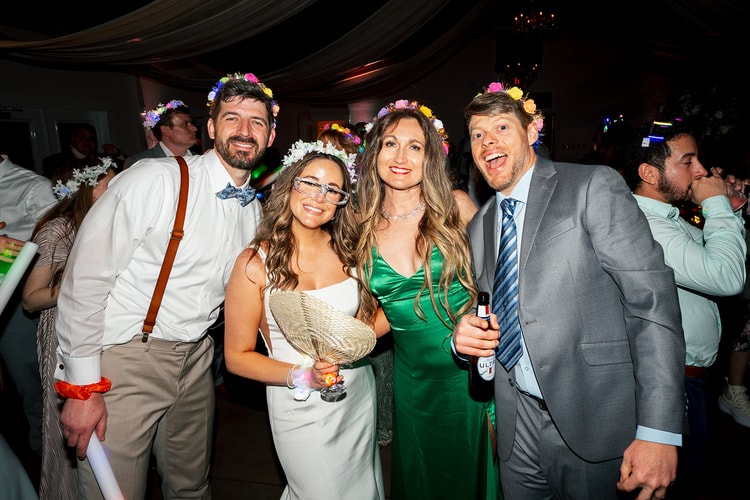 Couple posing with two guests, all wearing flower crowns and smiling at the camera during the late-night reception on the dance floor, wedding photography