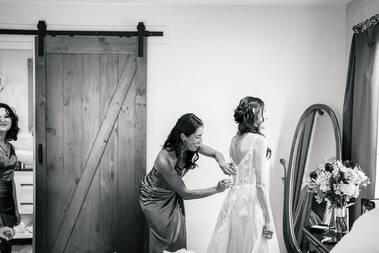 A helper fastens the back of Danielle's lace gown in the bedroom, black and white