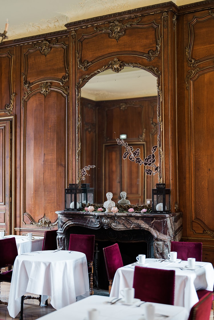 Morning light through velvet curtains on breakfast tables and crimson chairs in the dining room of Domaine du Château d'Ermenonville