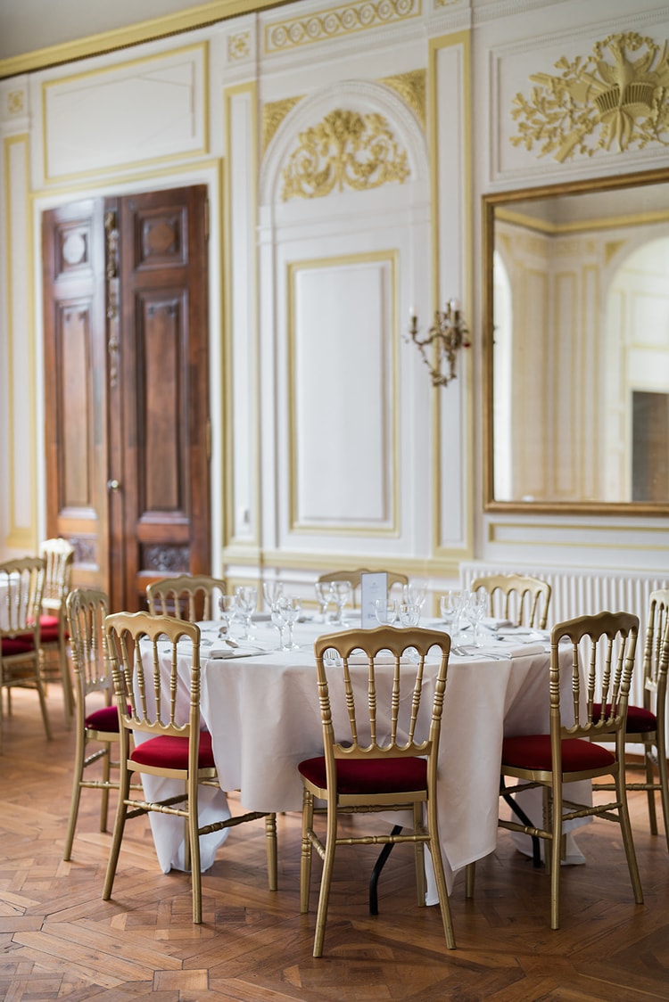 The yellow ballroom of Domaine du Château d'Ermenonville, round tables and gold chairs under a brass chandelier beside tall French windows