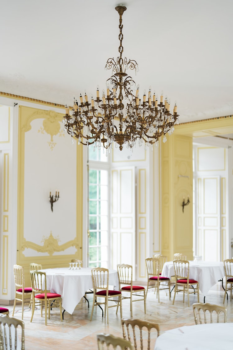 Tall French doors in the yellow salon of Domaine du Château d'Ermenonville framing the moat outside, flowers on a marble-topped commode
