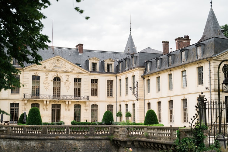 Turreted corner pavilion of Domaine du Château d'Ermenonville behind iron railings, white roses edging the lawn