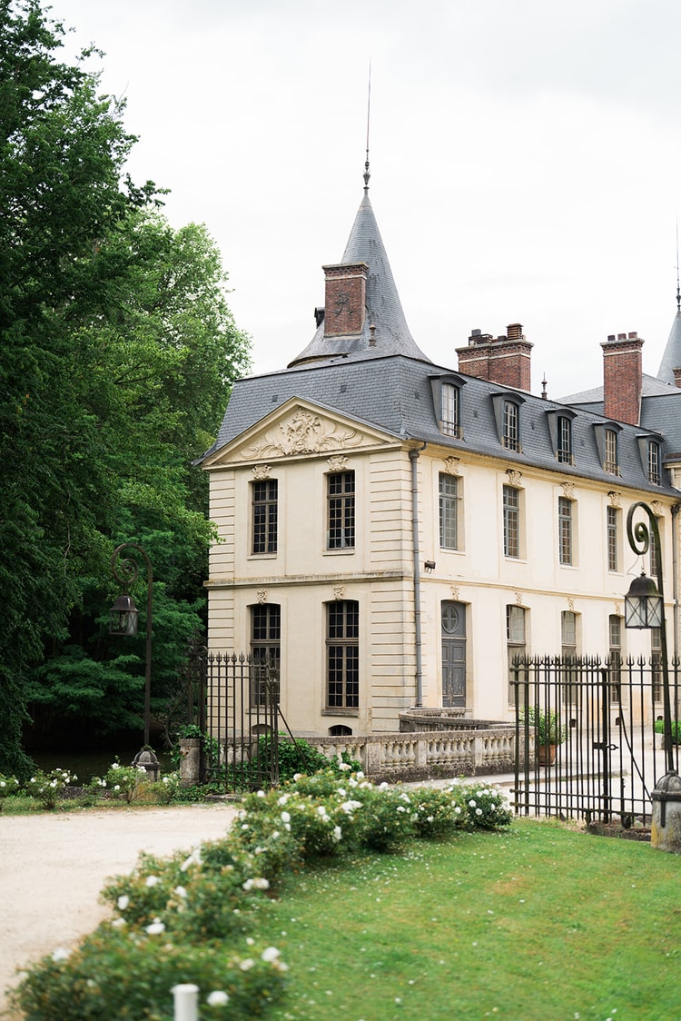 A slate-roofed pavilion of Domaine du Château d'Ermenonville standing over the still water of its moat, framed by trees