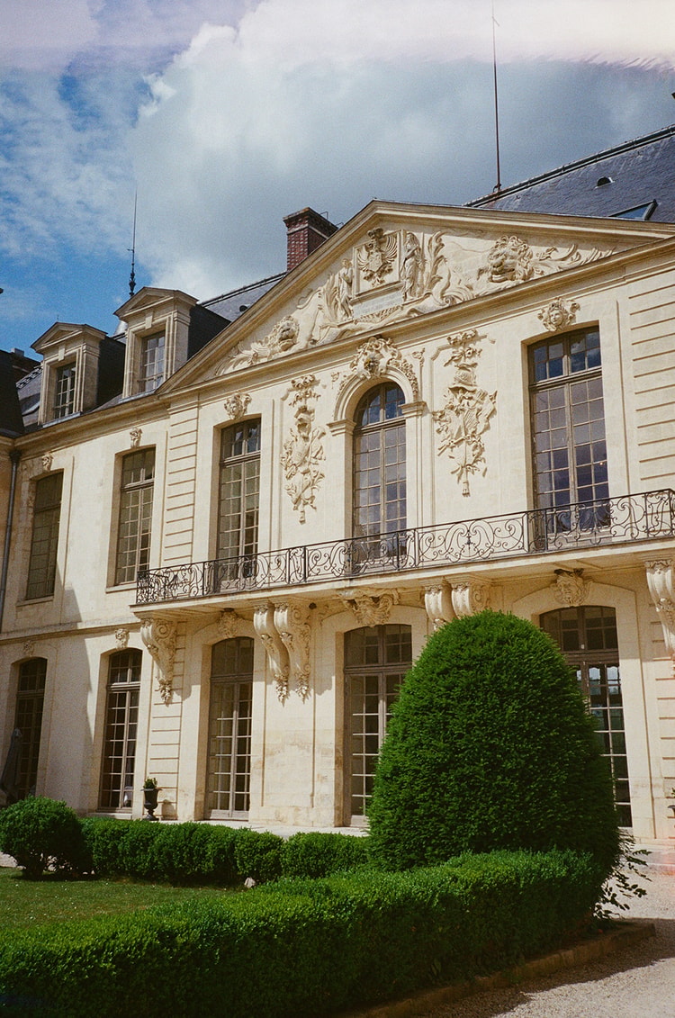 Blue sky and drifting clouds over the sculpted garden facade of the château at Ermenonville, France, shot on film with topiary in front
