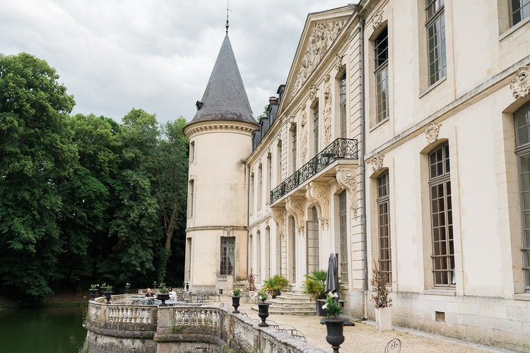 Moatside terrace of Domaine du Chateau d'Ermenonville with its conical tower, carved facade and flower-filled urns on the gravel