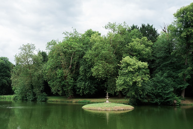 Tiered stone fountain on a tiny grass island in the still green water of the park at Ermenonville, France