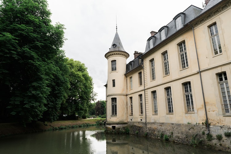 Turret and windows of Domaine du Chateau d'Ermenonville reflected in the still green moat, summer trees on the far bank