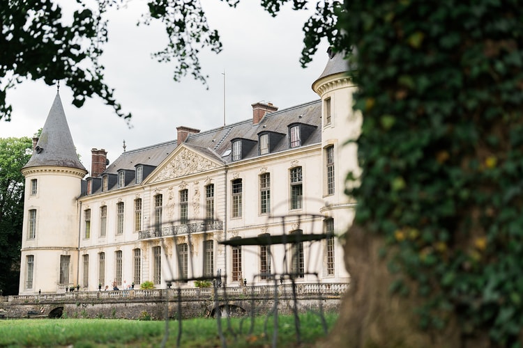 Sculpted pediment and twin turrets of Domaine du Château d'Ermenonville seen across the lawn, past an ivy-covered tree trunk.