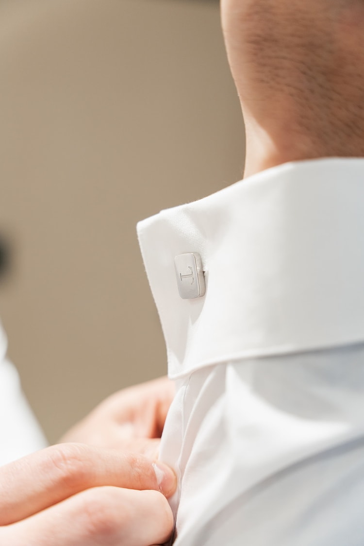 Close-up of a silver monogrammed cufflink being fastened on a white dress shirt cuff, wedding details