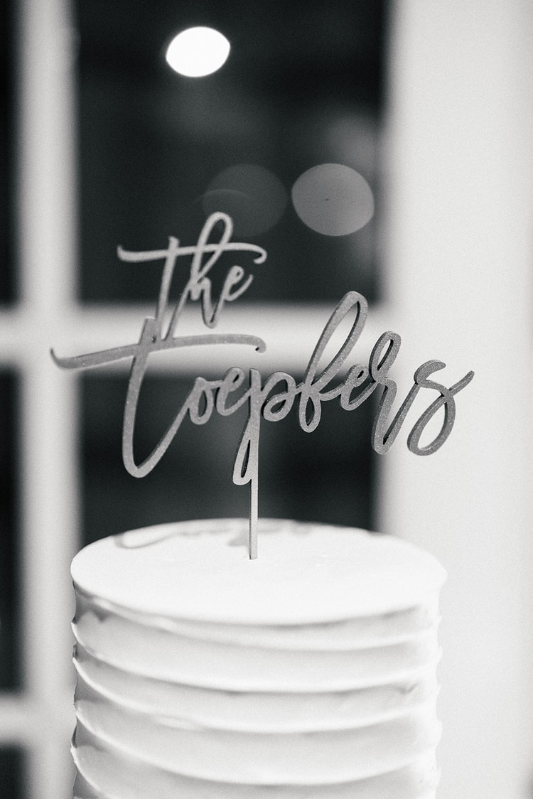 White tiered wedding cake topped with a custom calligraphy cake topper, black and white close-up, wedding details