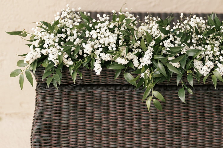 Baby's breath and eucalyptus garland draped along the top of a wicker bar or cabinet at the outdoor reception.
