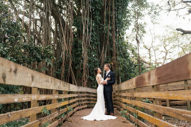 Bride and groom laugh together as they walk past wooden ceremony bench seating in an outdoor park