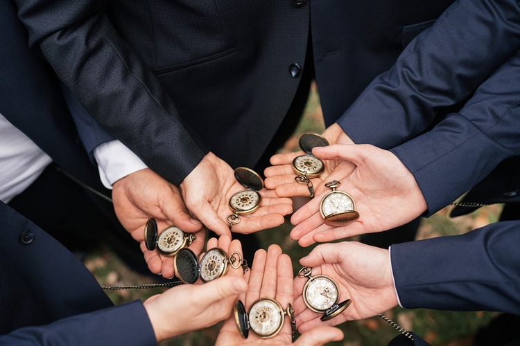 Groomsmen hold out open palms displaying matching antique pocket watches, a gift detail shot from above.